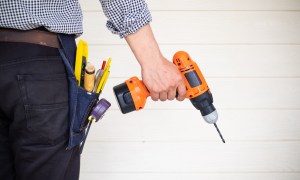 Person in a tool belt holding an orange drill