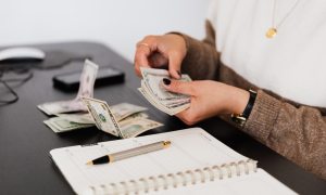 woman counting money next to notebook