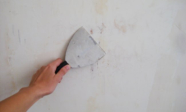 Person with putty knife patching drywall