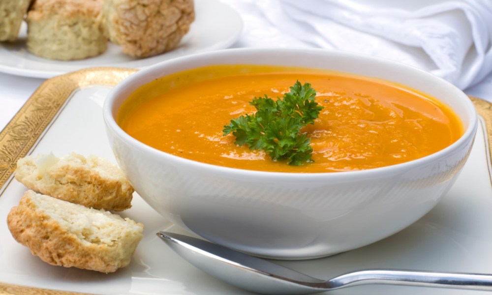 Carrot soup in a white bowl with a side of bread