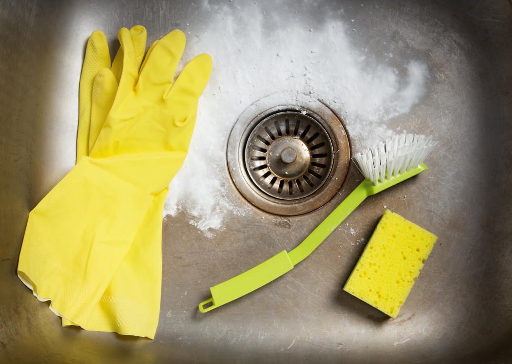 Rubber gloves, scrub brush, and sponge in a kitchen sink