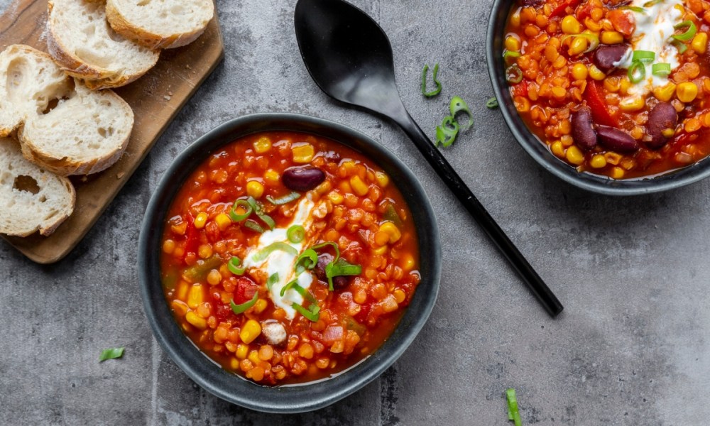 Two bowls of chili with a spoon and bread on a table