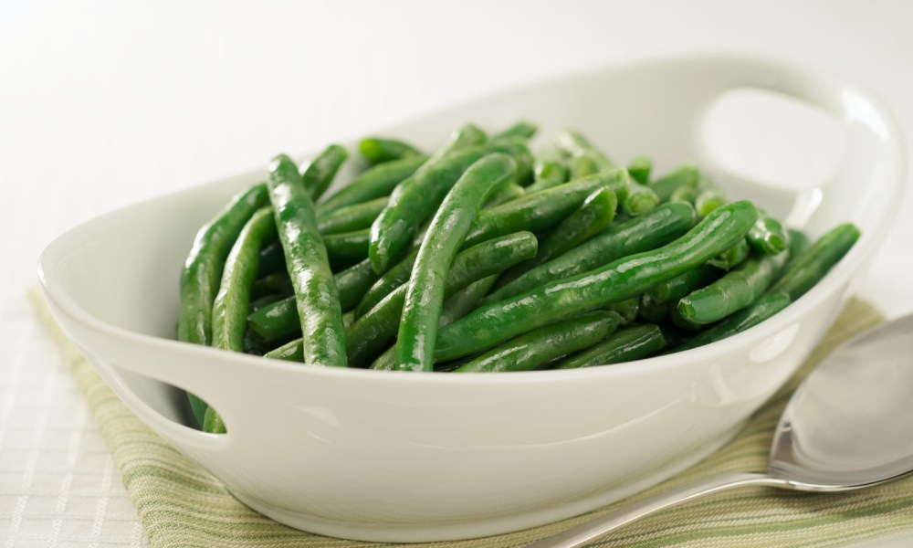 Steamed green beans in white bowl with serving spoon