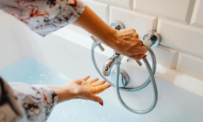 Woman testing hot water on bath faucet